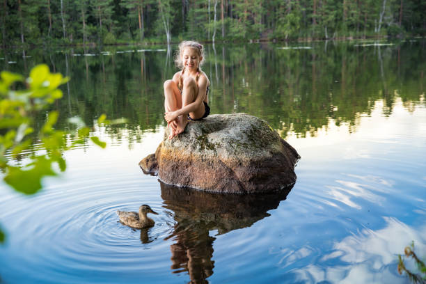 Cute little girl sitting on a rock in lake Cute little girl sitting on a rock in lake. Enjoying summer vacation. Child and Nature. Happy isolation concept. Exploring Finland. Scandinavian landscape. 2. Ideal for solo travelers stock pictures, royalty-free photos & images